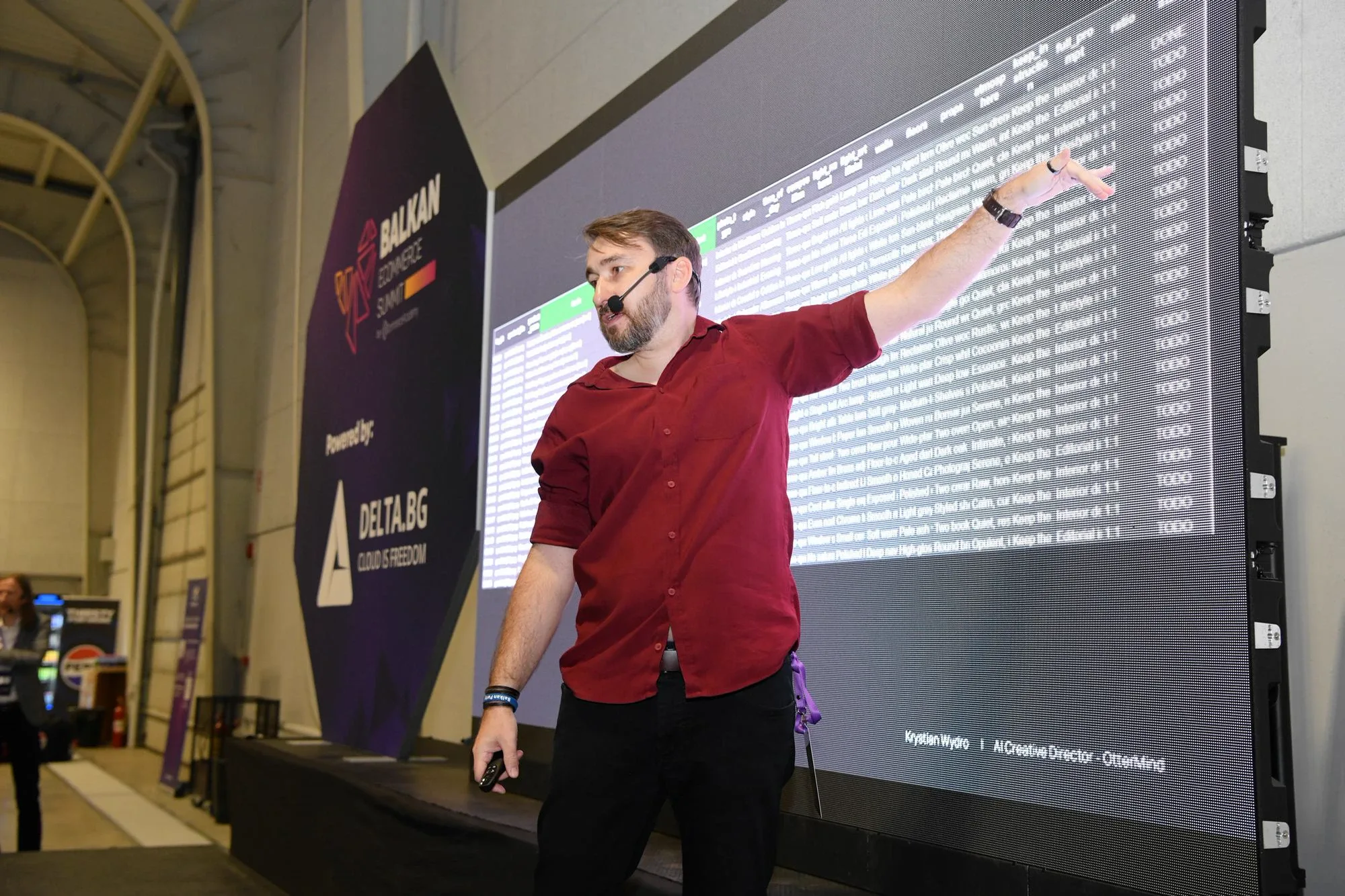 Krystian Wydro in a burgundy shirt pointing at a screen with a table on the DELTA stage during the Balkan eCommerce Summit 2026 in Sofia