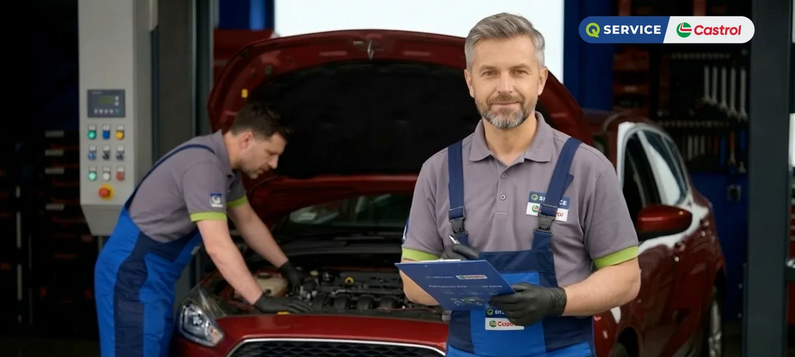A Q Service mechanic with a tablet in the workshop, another working under an open bonnet