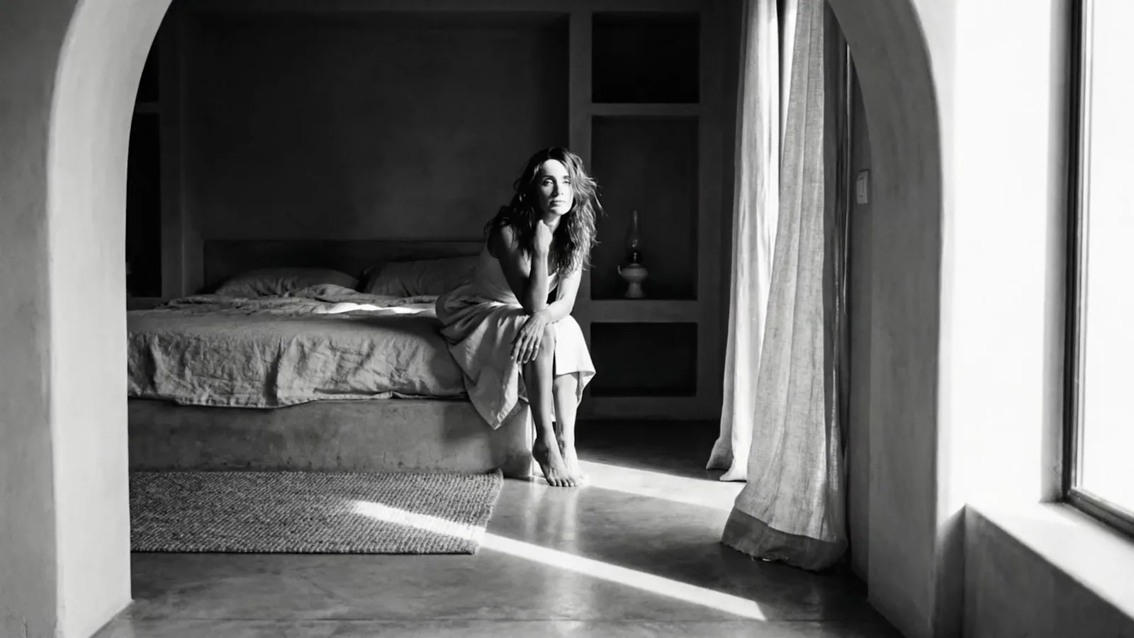 A woman sitting on a bed in a bedroom with an arched doorway