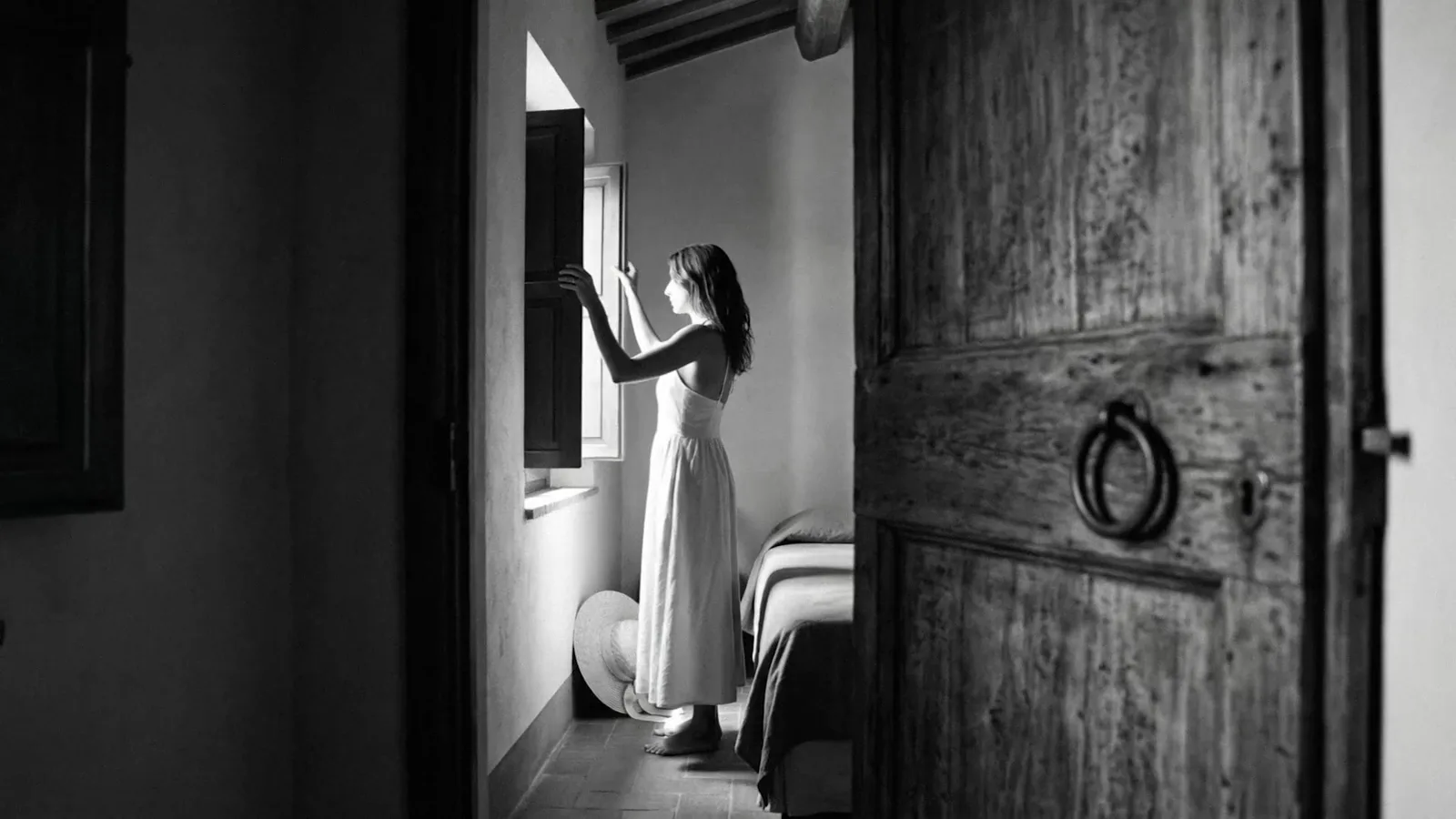 A woman by a window next to a heavy wooden door